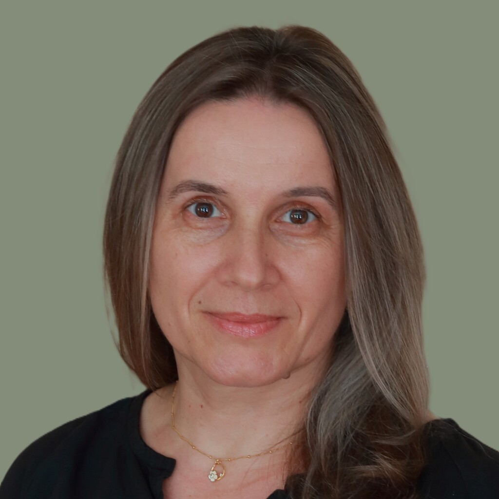 Headshot of Alla Armstrong looking at the camera while wearing a black shirt and gold necklace.