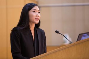 picture of Melany Sun-Min Park standing at a podium in front of a microphone