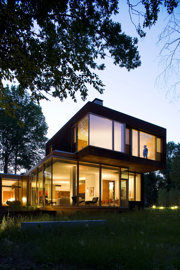 A two-story glass house with all the lights on inside.