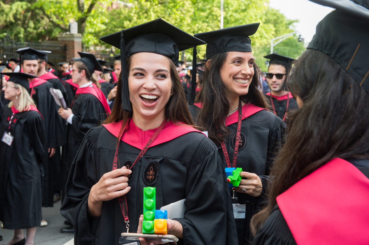 Students celebrate at Harvard Yard Commencement in black and crimson regalia and holding colorful blocks.