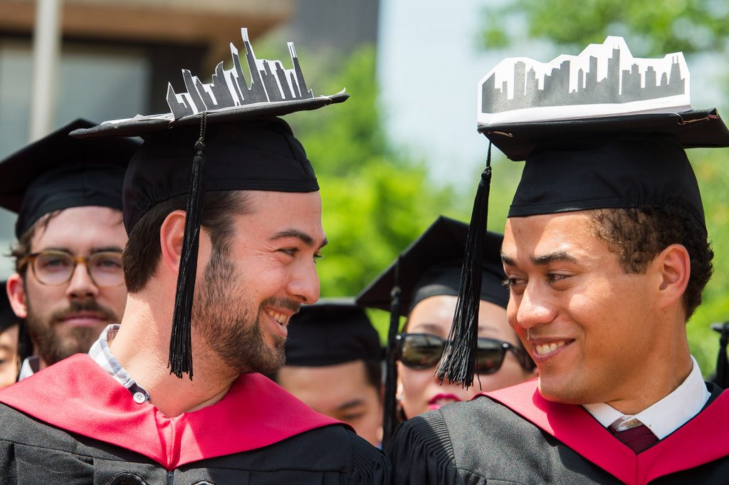 Two graduates look at each other and smile while wearing their regalia.