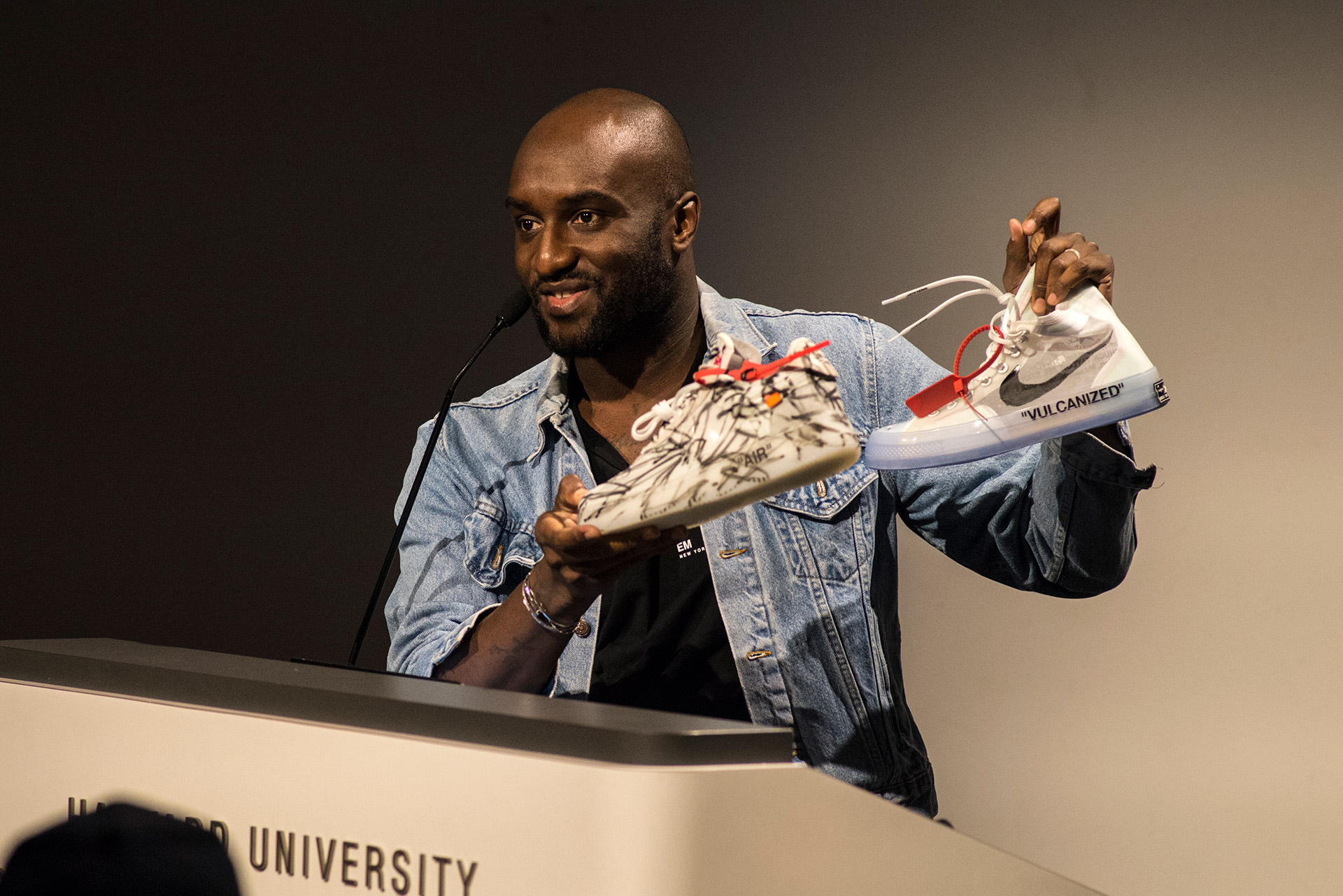 Virgil Abloh holds up two pairs of sneakers at the GSD lecture podium