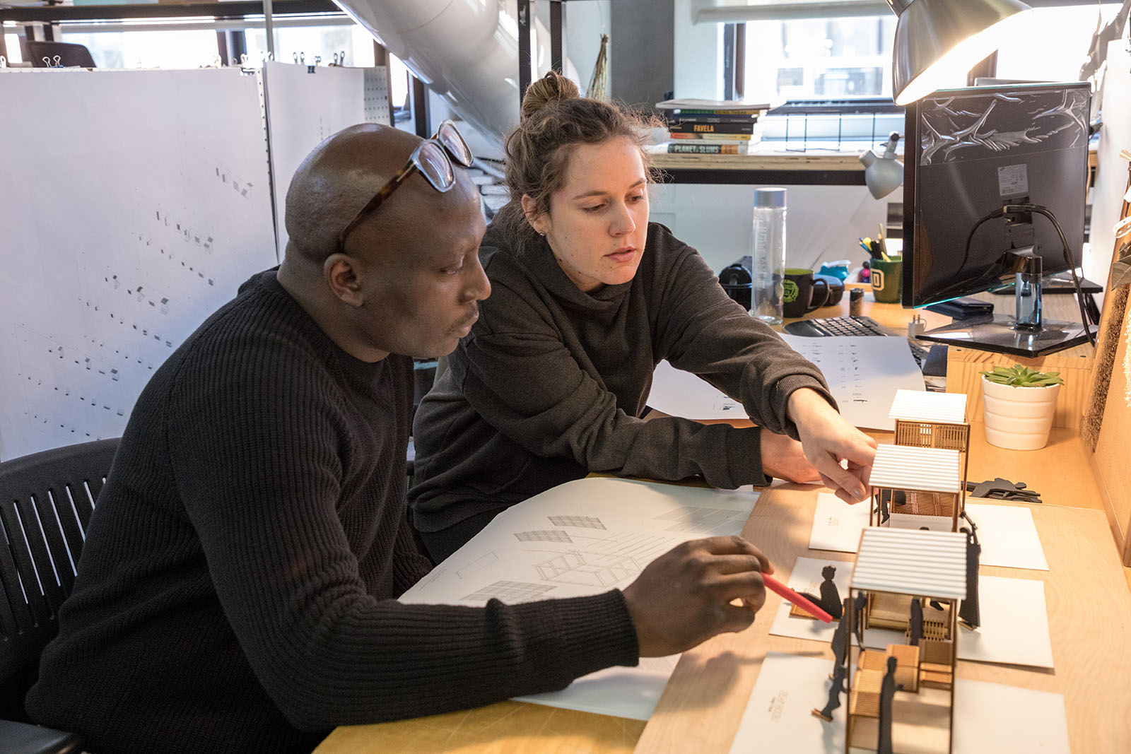 A faculty member and student sit at a desk and look at a project together.