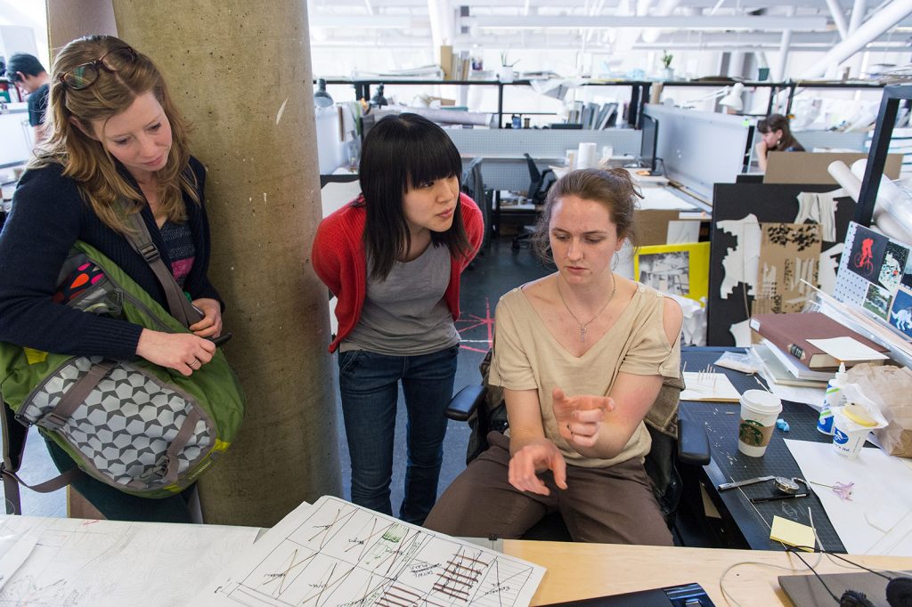 Three people talk around a desk.