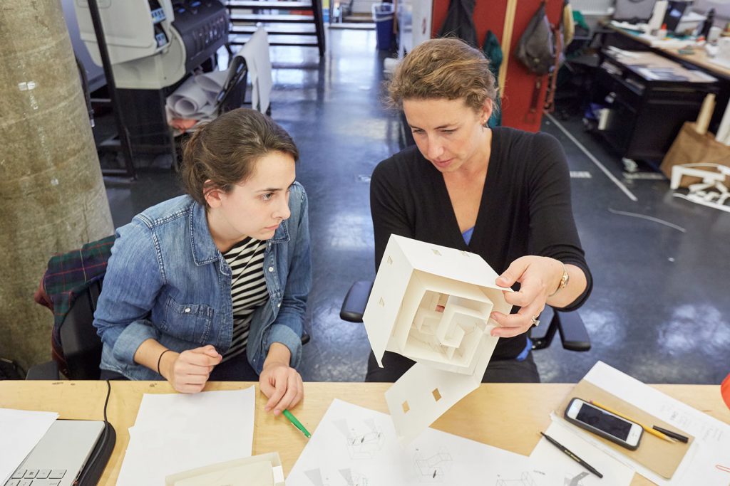 A student and faculty member look at a work in progress while sitting at a desk in the Trays.