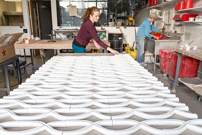 A student stands at the end of a table covered with ceramic pieces.
