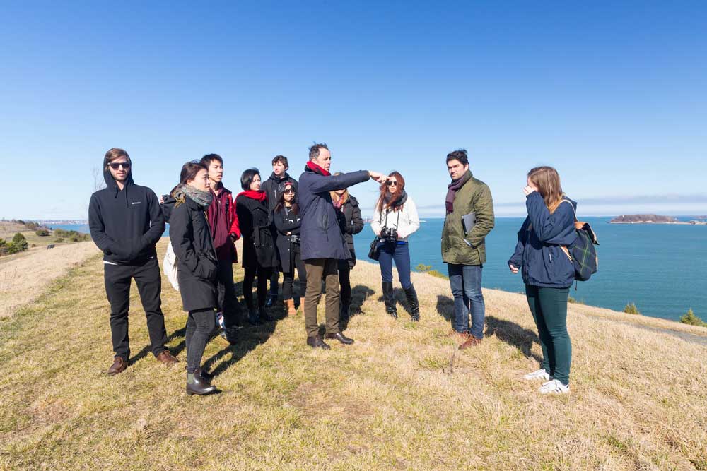 Students stand around a faculty member near the seaside.