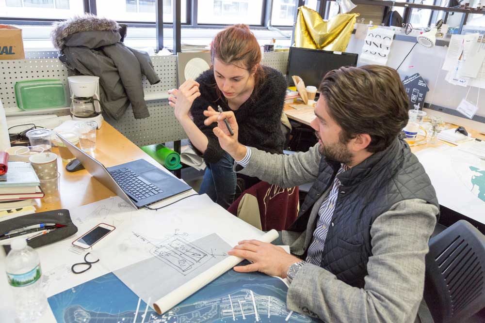 Two people collaborate on a document while sitting at a desk together.
