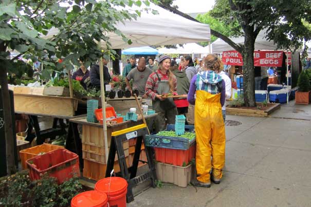 People mingle at a farmer's market tent.