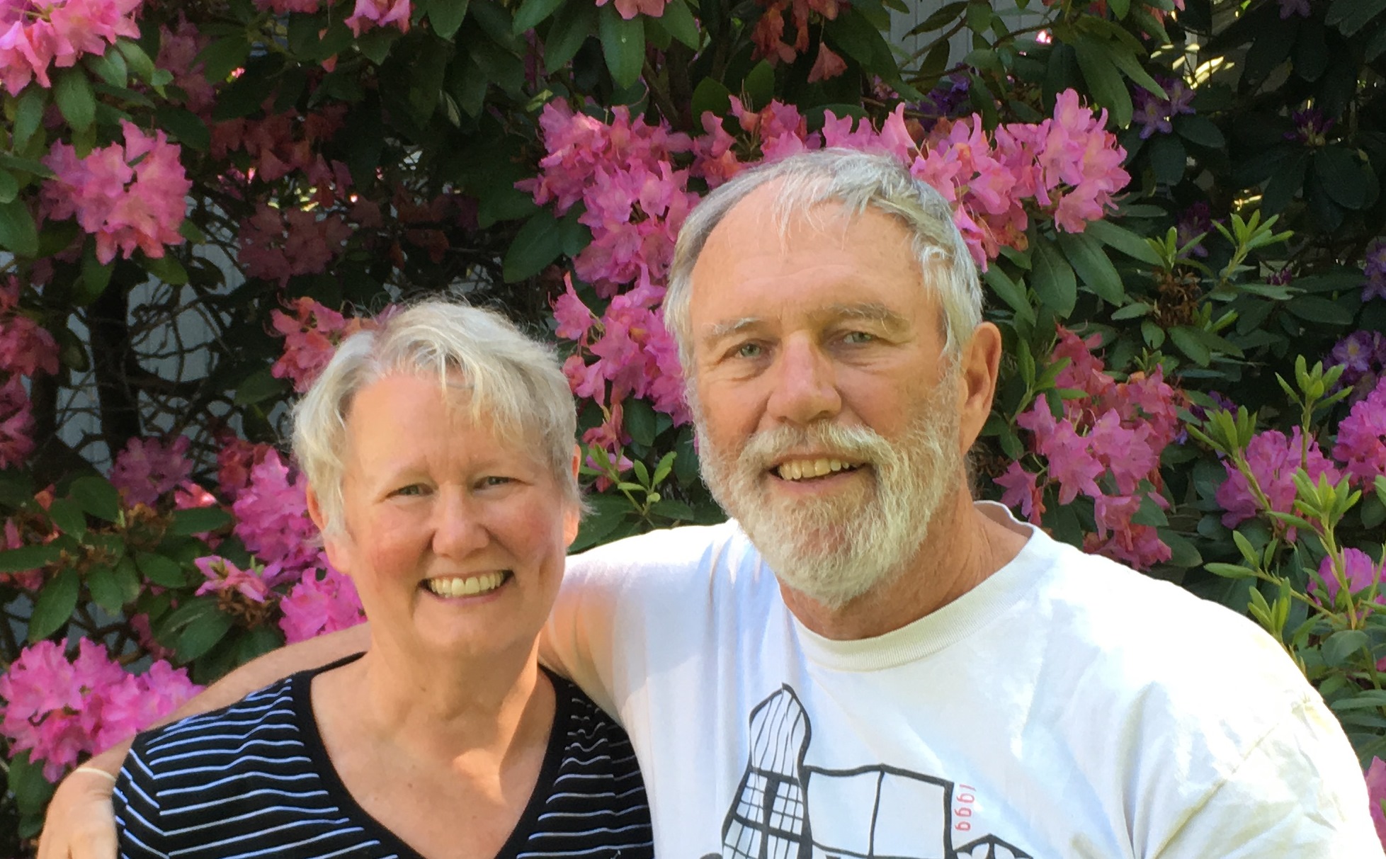 Photo of a couple facing the camera with flowers in the background.