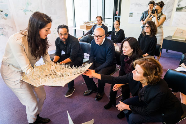people cluster around an architectural model held by a student
