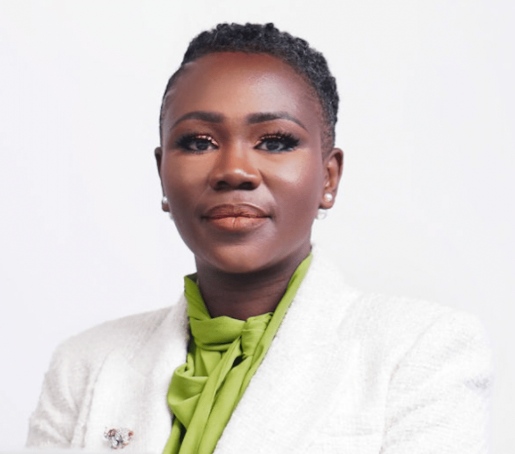 Naisha Bradley, a Black woman, is wearing a white blazer with a green blouse on a white background and is smiling into the camera.