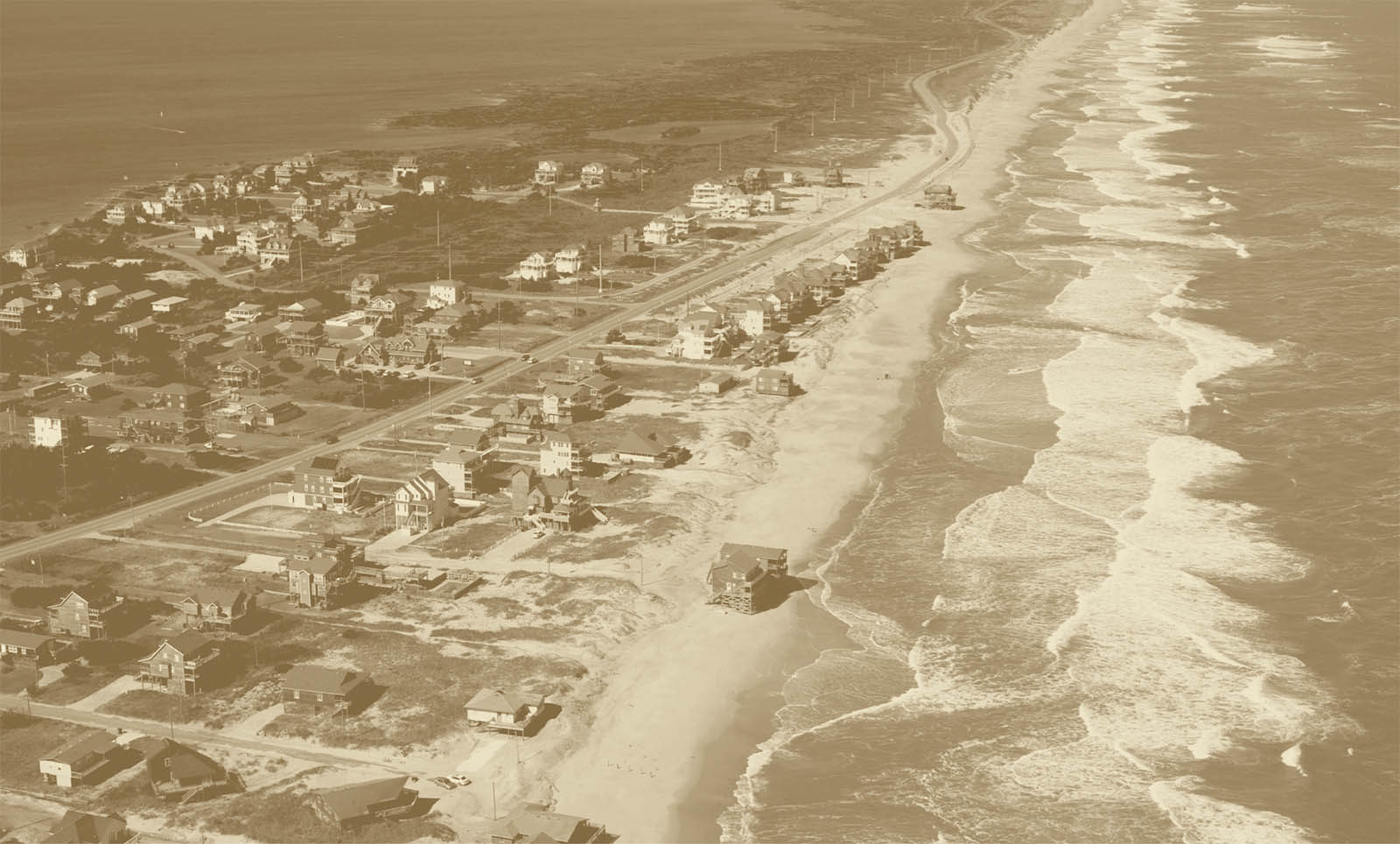aerial image of housing on a narrow peninsula with waves crashing against the beach