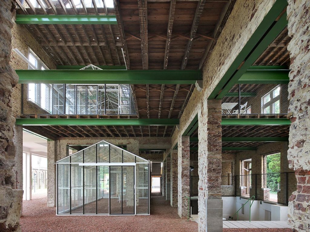 Small glass house inside a large brick, concrete and steel warehouse