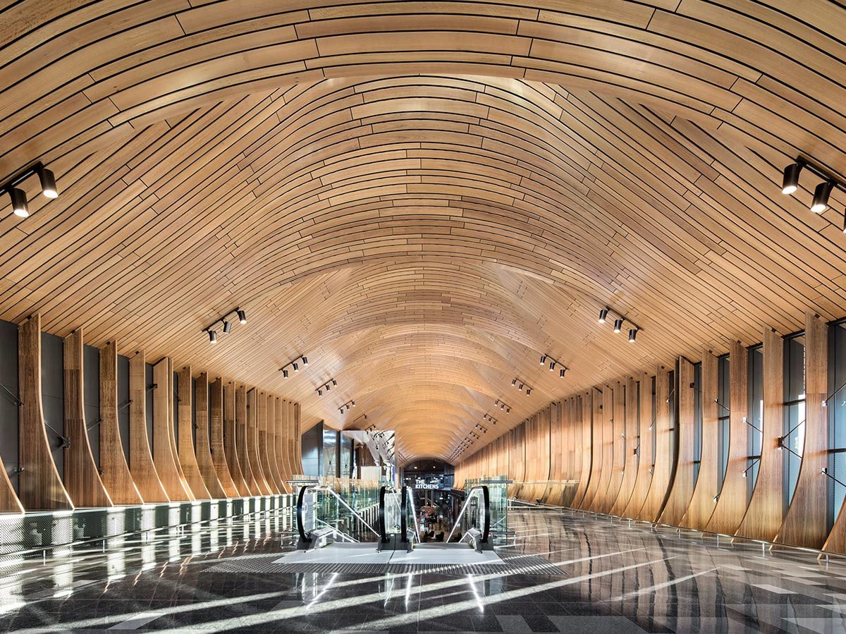 Large hallway with wooden ceiling and escalator descending into the floor