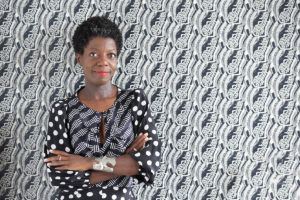 Headshot of Thelma Golden, who wears a black-and-white dress and stands in front of a patterned backdrop.