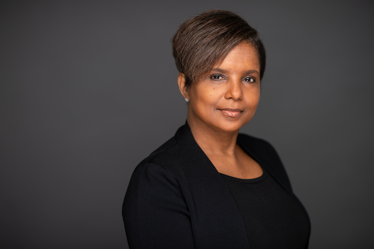 Headshot of Sheila Foster, a black woman who has short brown hair and wears black. The background is gray.