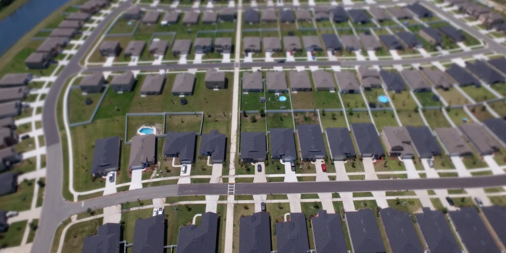 An overhead view of a suburban neighborhood with many houses, all with roofs in different shades of gray.