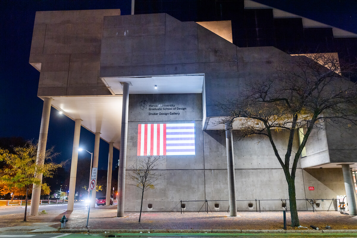 Gund Hall at night with projection illuminated on the side of the building.