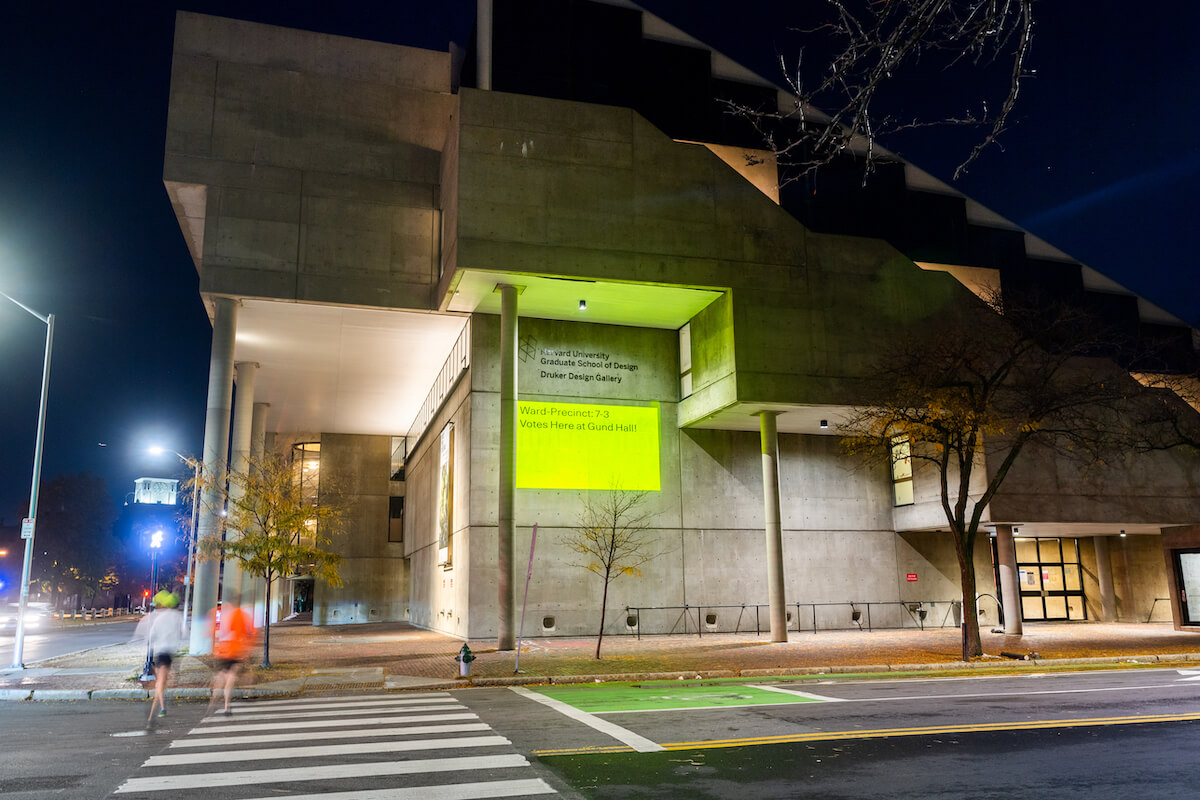 Gund Hall at night with projection illuminated on the side of the building.