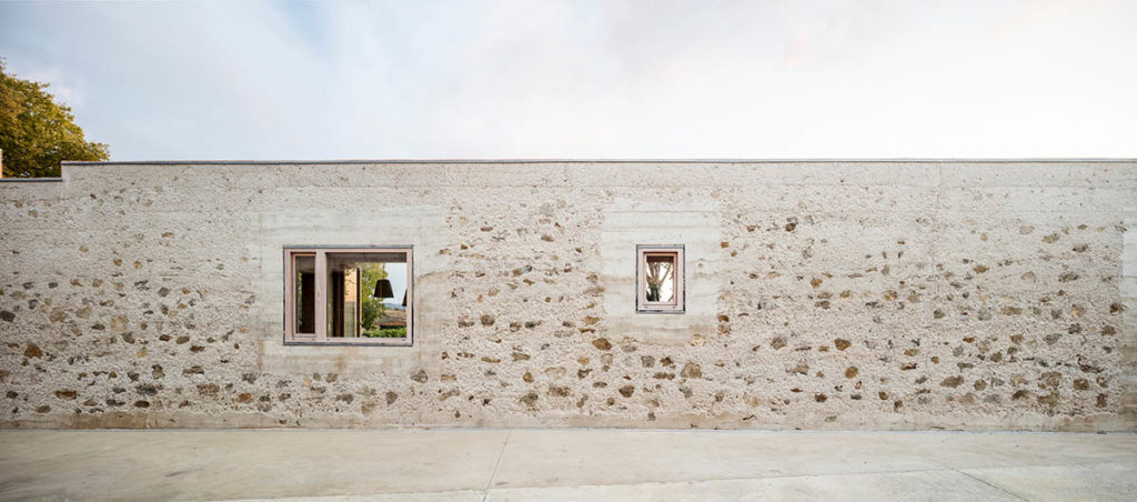 Image of the wall of a building, with two windows and rocks embedded in the wall.