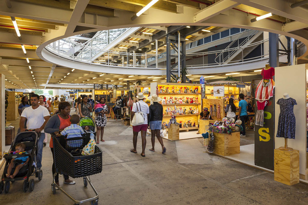 A multi-level marketplace with many people walking around. In the ceiling there is a circular opening, allowing people to see upper floors.