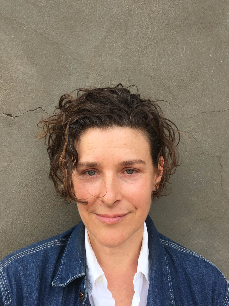 Headshot of Zoe Leonard, who wears a blue denim jacket and white shirt.