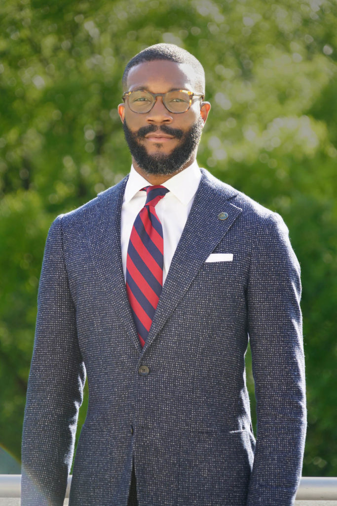 Headshot of Mayor Woodfin, who wears a gray suit, white shirt, and red and blue striped tie. He also wears glasses.
