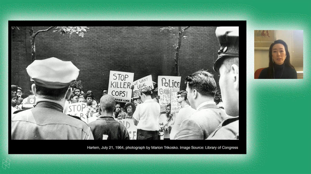 Screenshot of a virtual event. Rebecca Choi appears in a small square on the right and wears a black turtleneck shirt. A larger rectangle contains her PowerPoint presentation, which shows a black-and-white photograph from a protest, where a sign reads "Stop Killer Cops." Rebecca and her PowerPoint are surrounded by a green background.