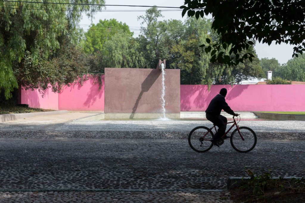 Image of man riding bike (silhouette) in front of pink Barragan wall