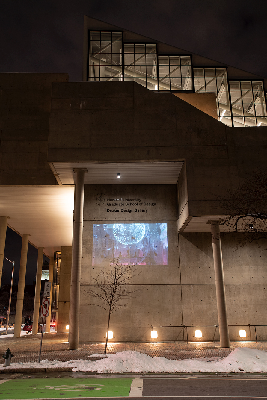 The Cambridge Street facade of Gund hall at night, showing the film “Floating Between Borders… or, Perhaps, an Earth Without Borders” projected on the wall.