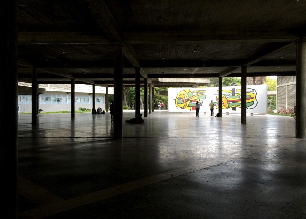 Image of dark interior looking to brightly lit exterior of the building, a colorful mural wall is at the distance