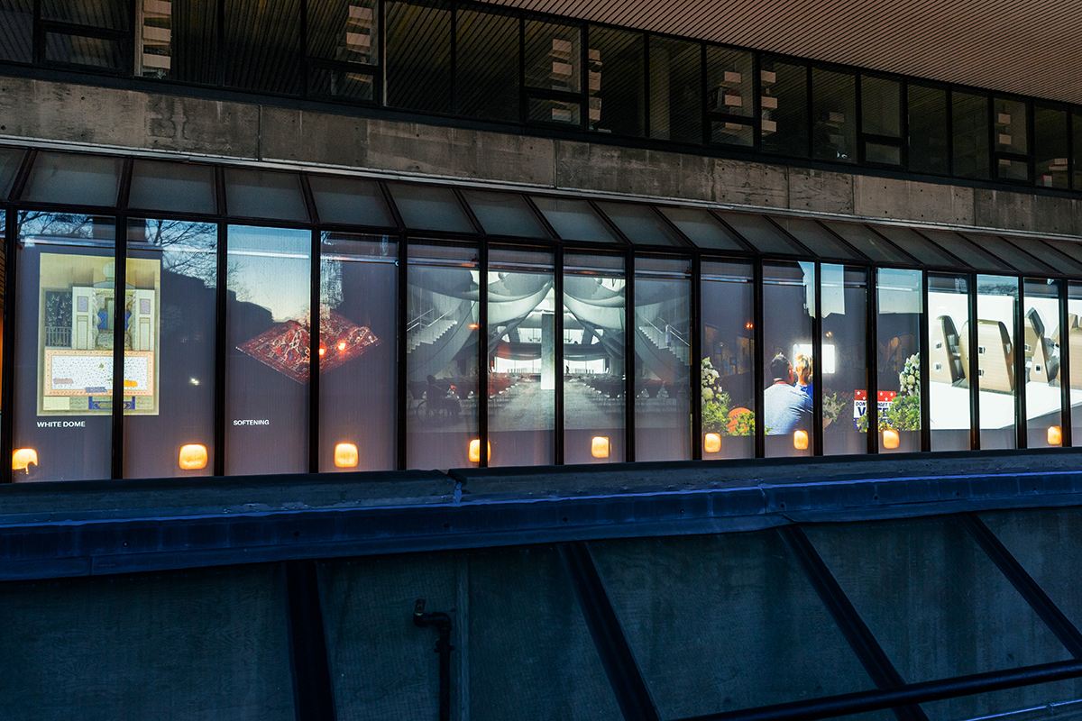 The Quincy Street facade of Gund Hall at night, showing four projections displayed in the windows.