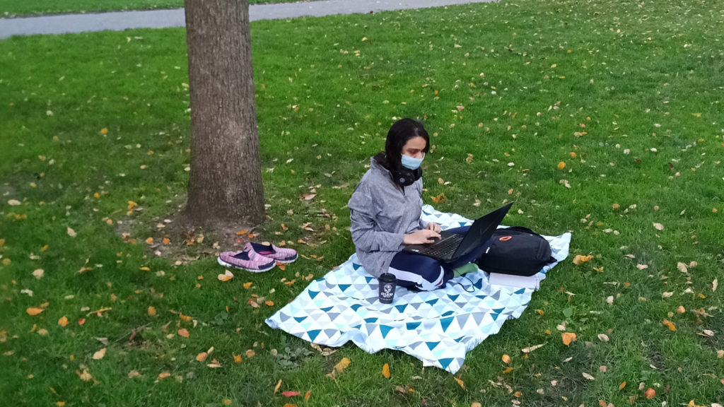 Image of Nupur sitting on a blanket on a field studying on her laptop