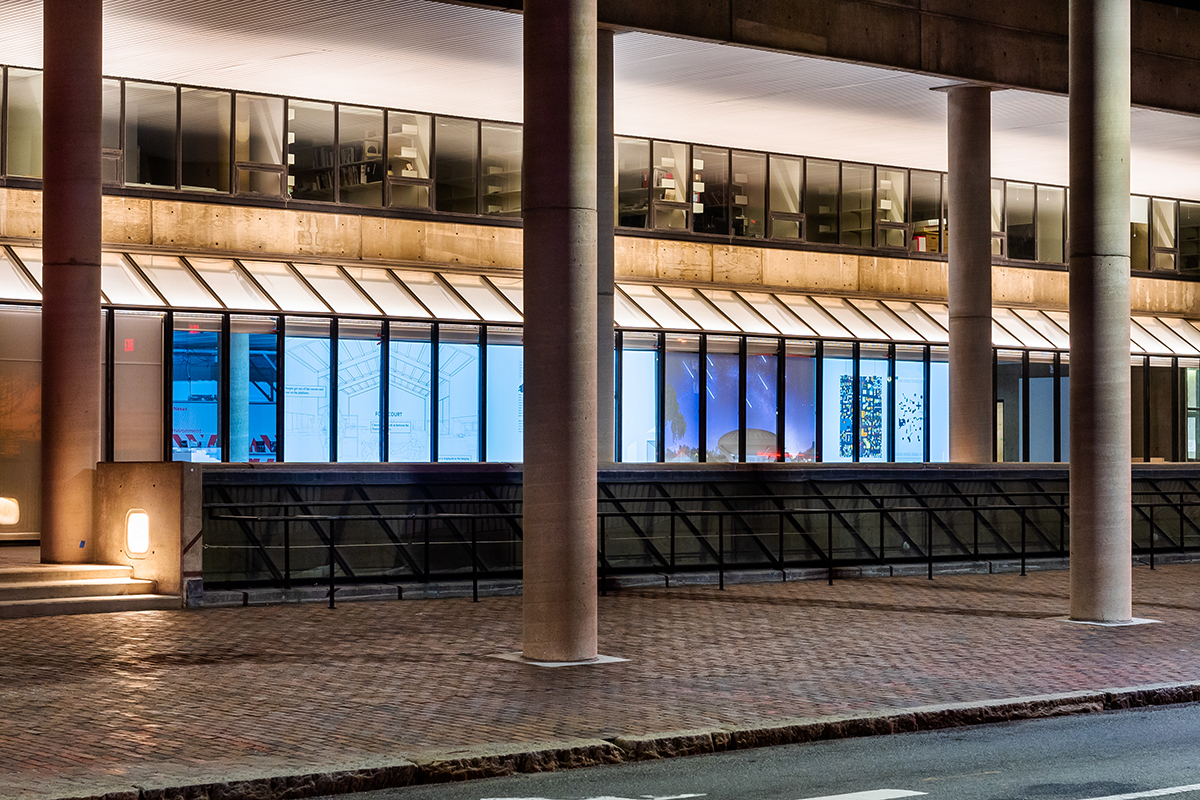 The Quincy Street facade of Gund Hall at night, showing four projections displayed in the windows.