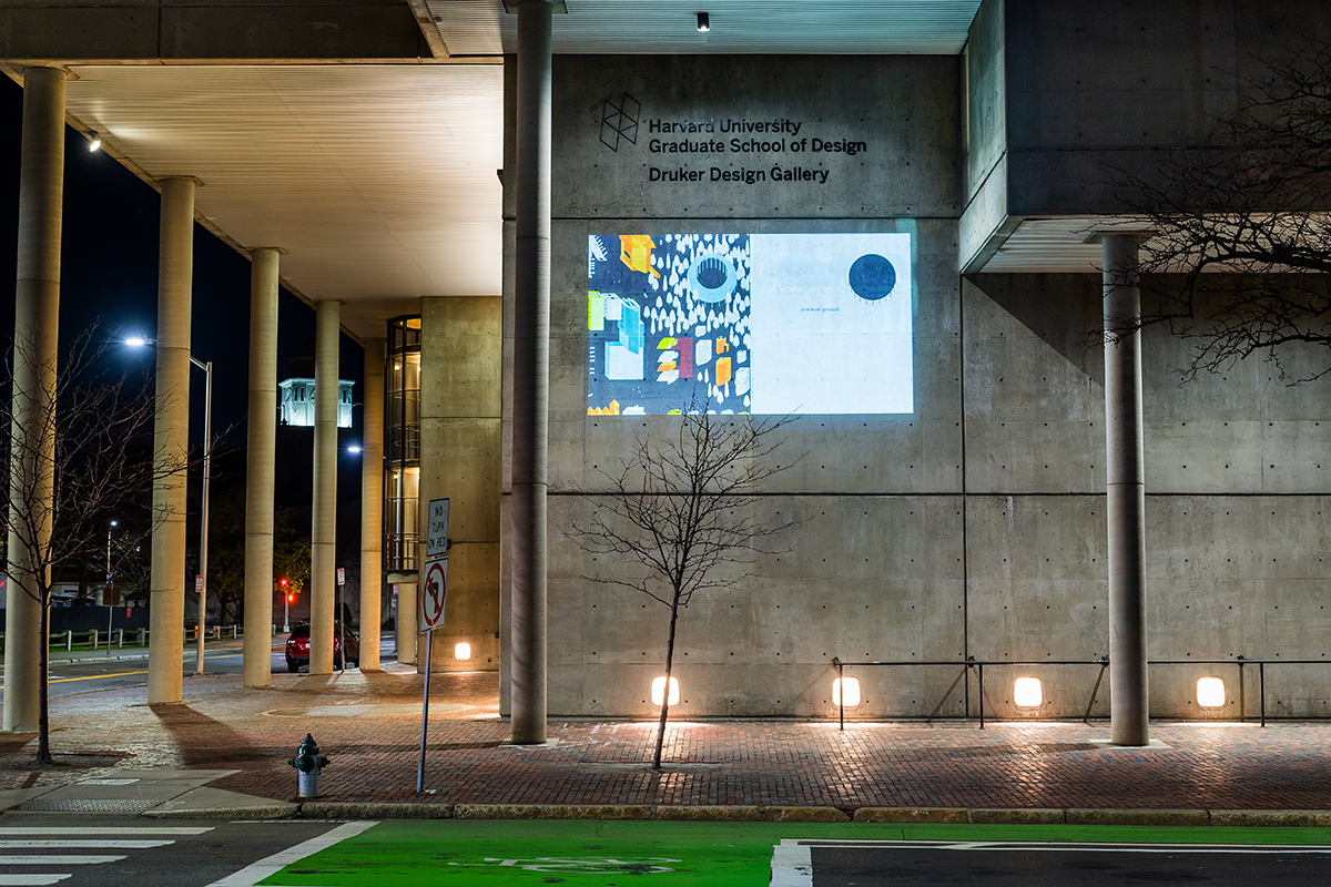 The Cambridge Street facade of Gund Hall at night showing a projection of a colorful map of a city.
