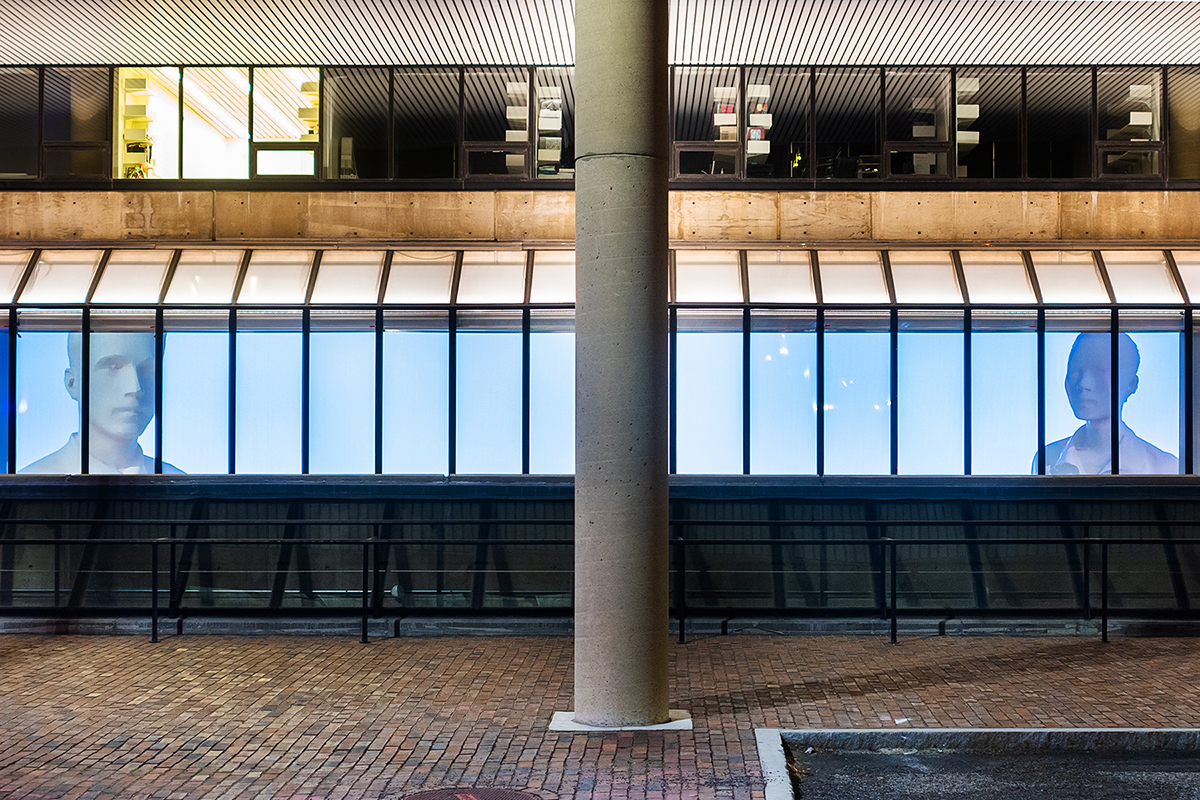 The Quincy Street facade of Gund Hall, showing a projection of two people's faces, one at either end of a large expanse.