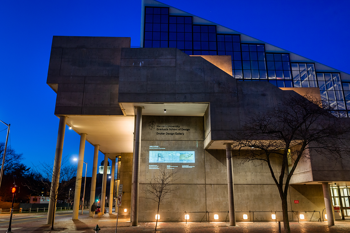 The Cambridge Street facade of Gund Hall at night, showing a projection about Landscape Architecture welcome kits.