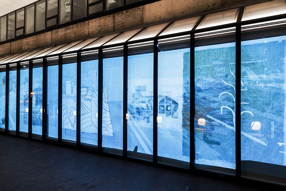 The Quincy Street facade windows of Gund Hall at night, showing a projection of the Landscape Architecture welcome kits.