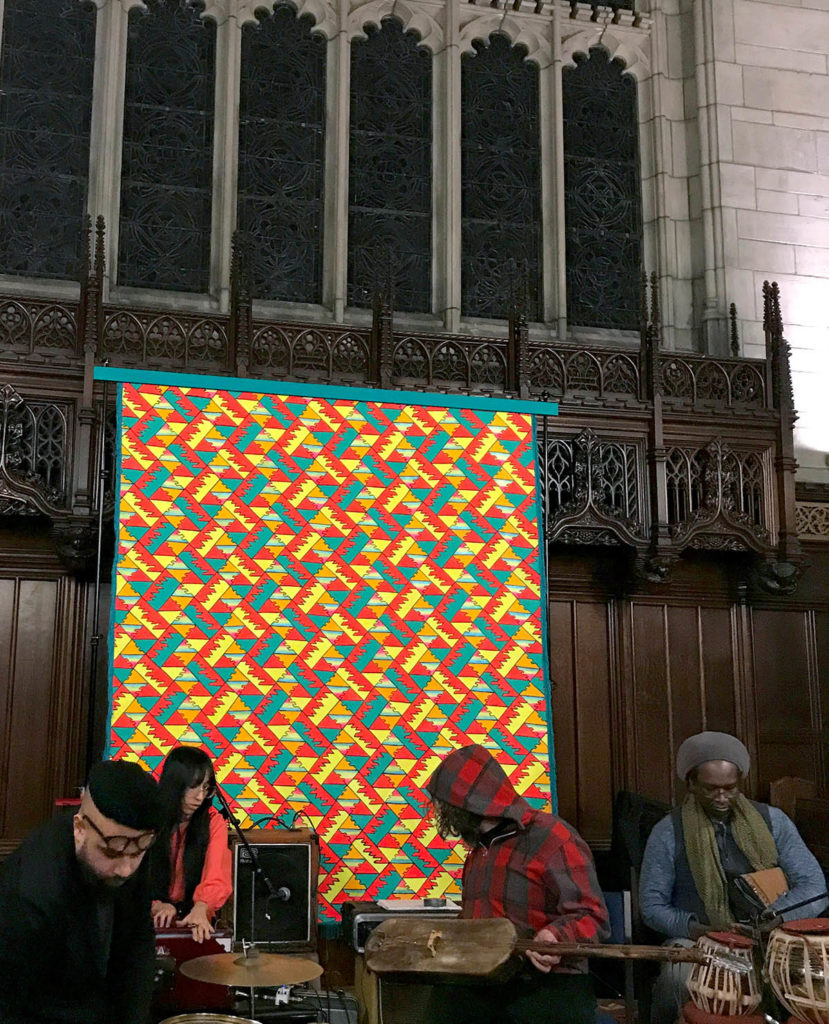Image of musicians in the Natural Information Society, who are playing in front of a colorful geometric backdrop.