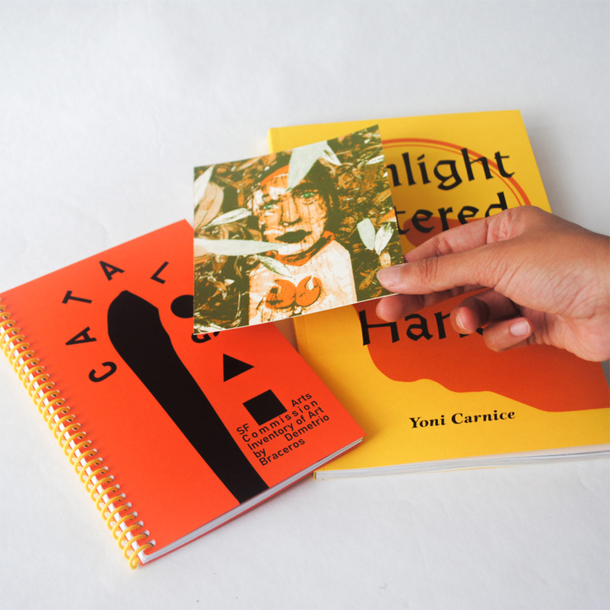 Yoni Carnice's book with a catalog and a hand holding a post card