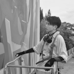 Zhanliang Chen holding a spray paint can in front of a mural 