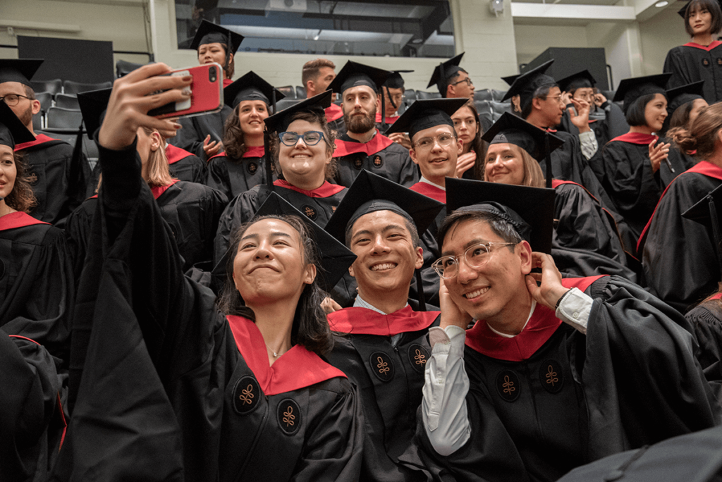Graduates wearing commencement robes pose for a selfie.