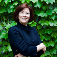 Headshot of Diane Davis, who wears a black shirt and stands against a backdrop of green leaves.