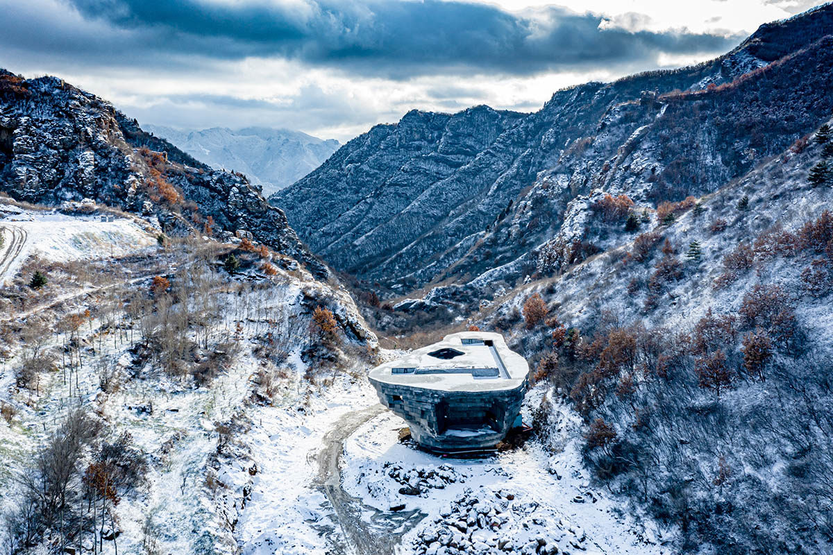 Photograph of a building sitting in a snowy valley, surrounded by mountains.