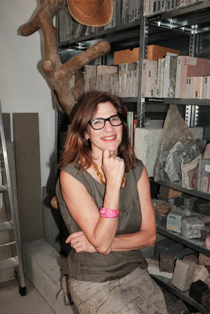 Headshot of Robin Wonigrond, who stands in front of a shelf which holds many rocks. She wears glasses and a gray shirt. 