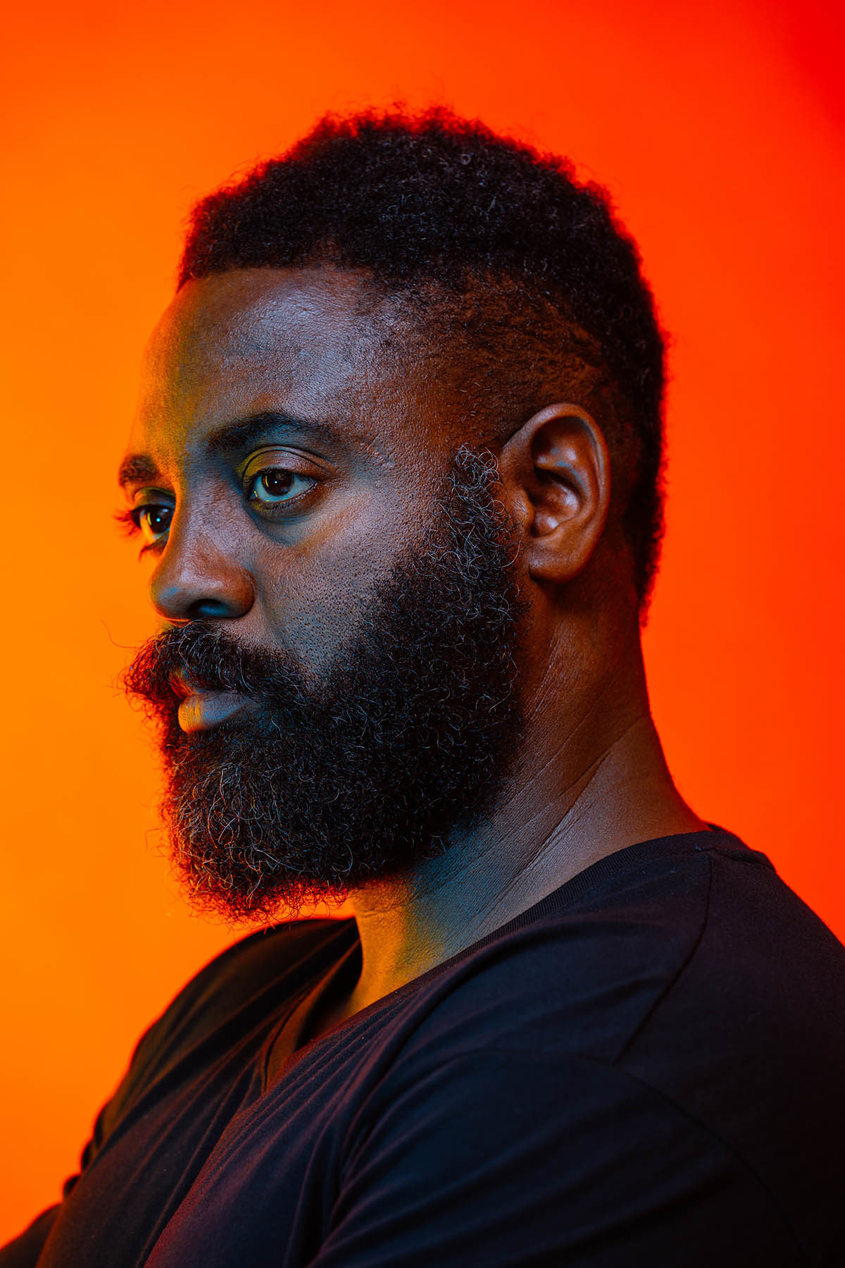 Headshot of Reginald Dwayne Betts, who wears a black shirt and stands in front of a bright orange background.