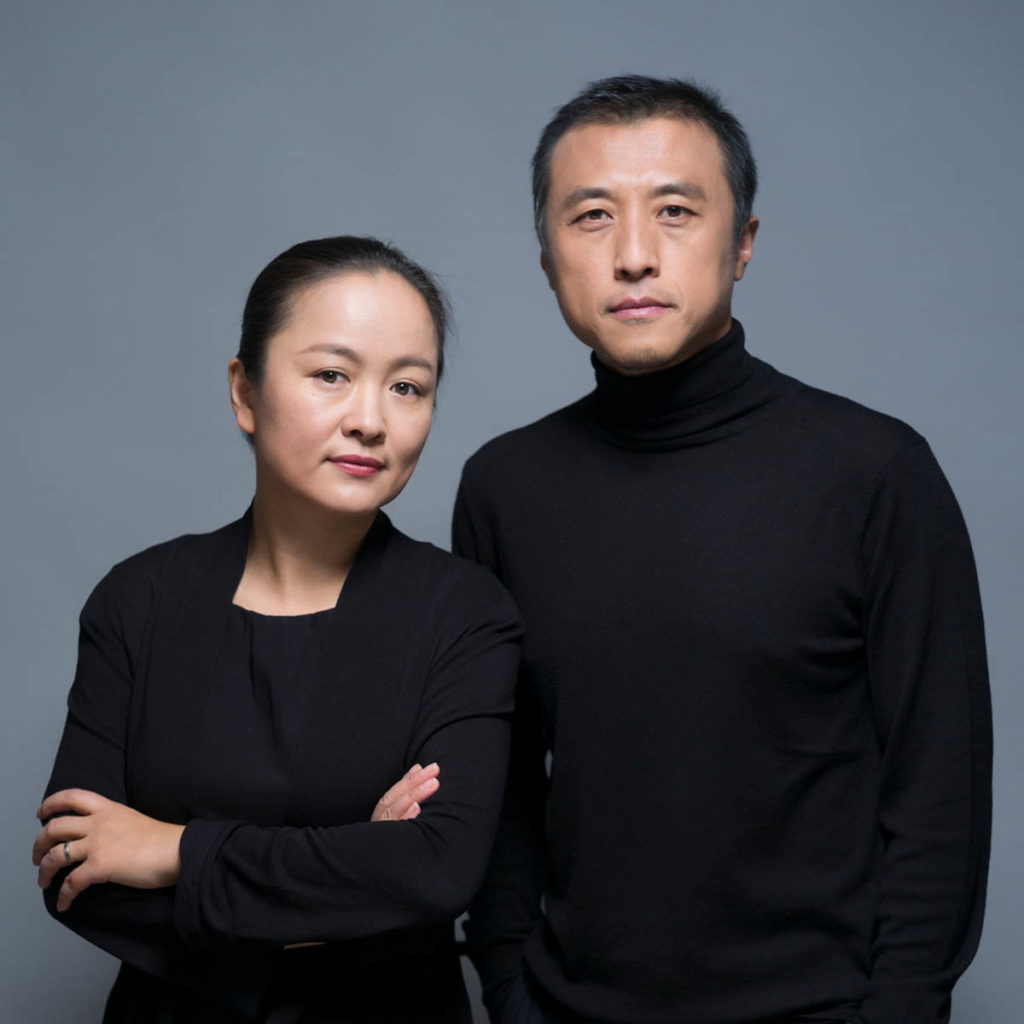 Headshot of Li Hu and Huang Wenjing, who both wear all black and stand against a gray background.