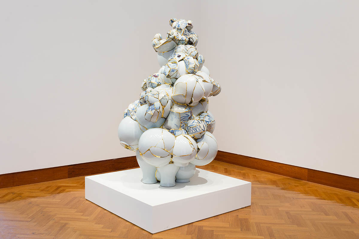 Photograph of a bulbous sculpture on a white platform in a white-walled room, with brown wood flooring.