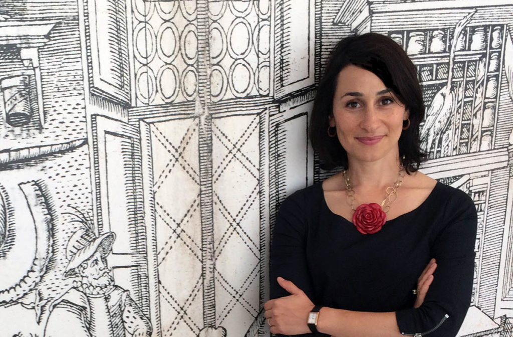 Headshot of Daniela Bleichmar, who wears a black top and a necklace with a large red flower.